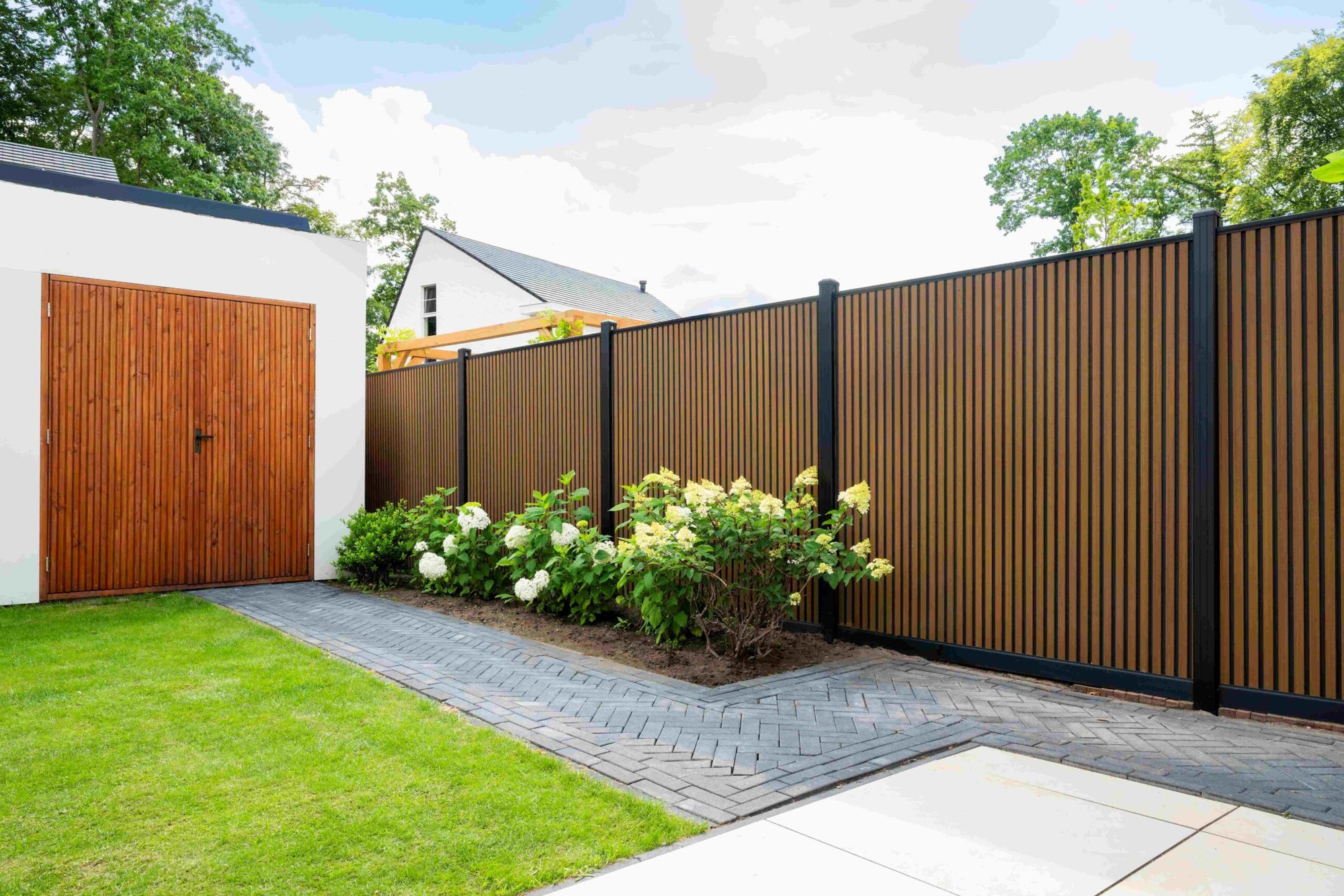 Moderne achtertuin met een dichte composiet schutting in houtlook, een border met witte hortensia en een terras van lichte tegels