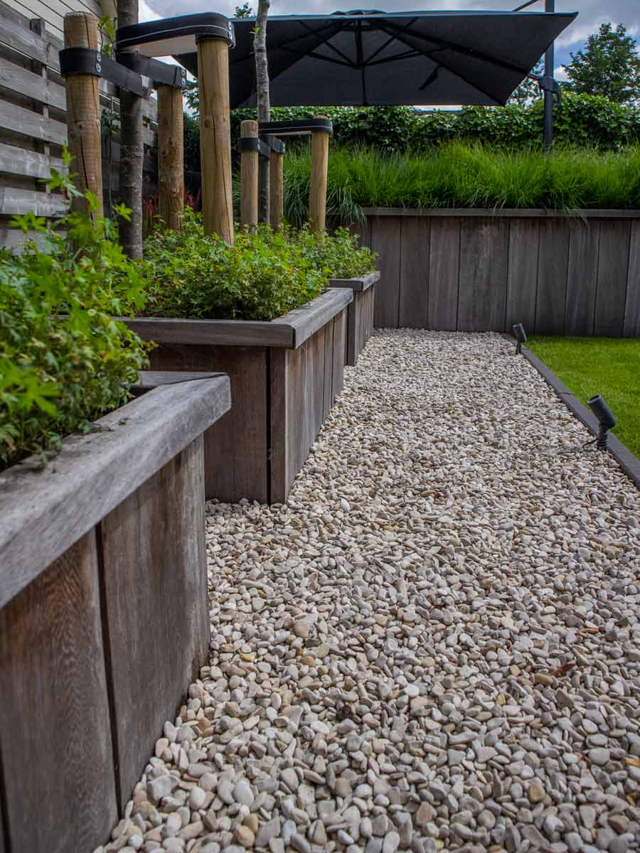 Tuin met Castle-grind langs houten verhoogde borders en beplanting