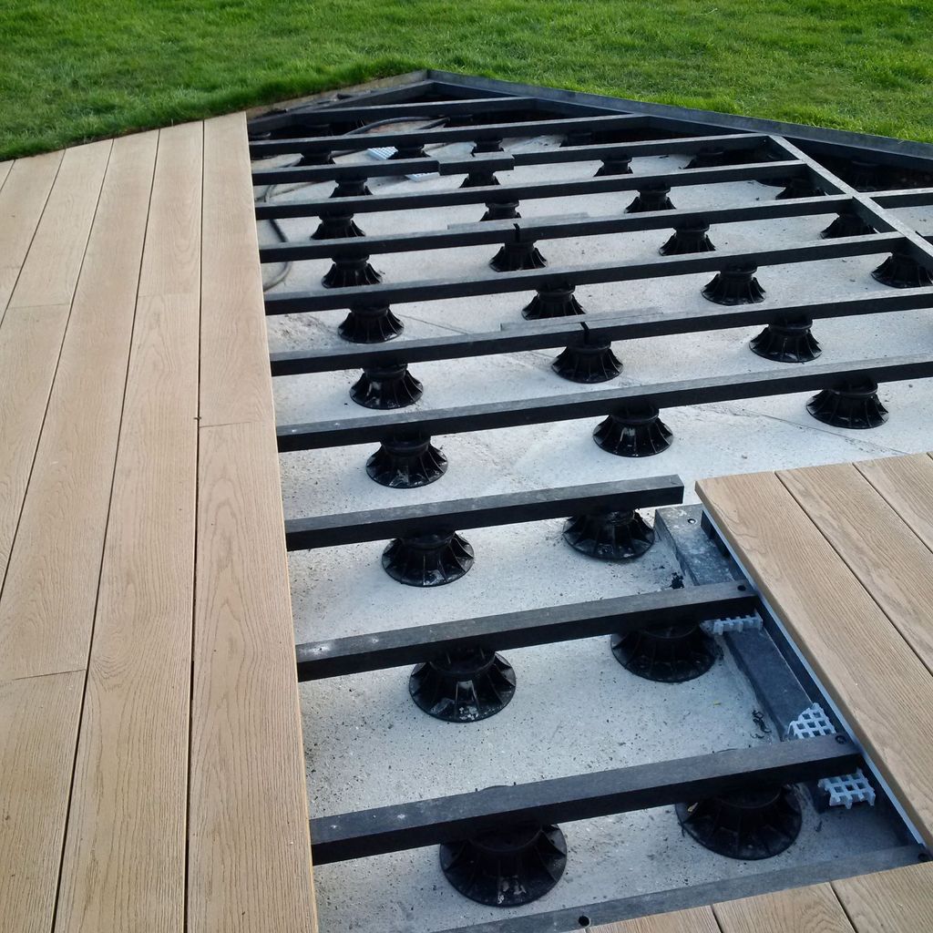 Millboard vlonder in aanleg met zwarte onderliggers op verstelbare dragers boven een vaste ondergrond