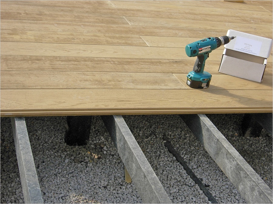 Millboard terrasplanken gedeeltelijk gemonteerd op kunststof onderliggers boven een grindbed